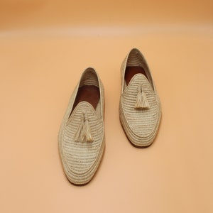 May include: A pair of beige woven leather loafers with tassels. The loafers are made of a natural material and have a casual, summery style.