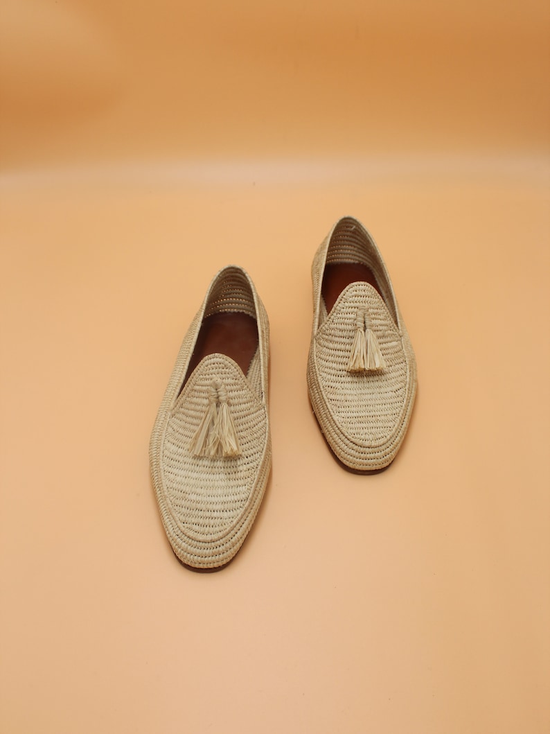 May include: A pair of beige woven leather loafers with tassels. The loafers are made of a natural material and have a casual, summery style.