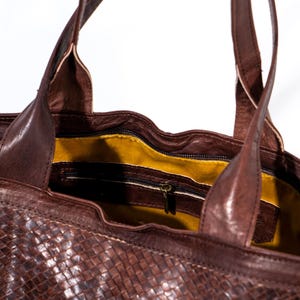 Puede incluir: Un bolso tote de cuero marr&oacute;n con un patr&oacute;n tejido. El bolso tiene un bolsillo con cremallera en el interior y un forro amarillo.