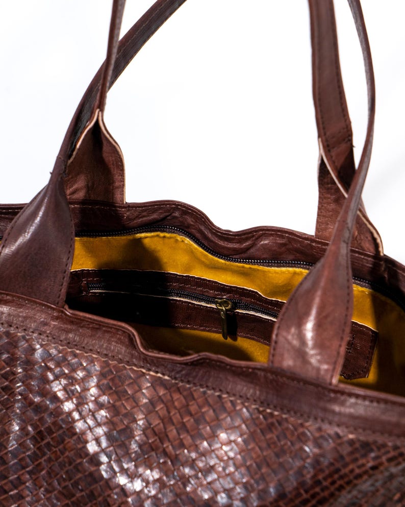 Puede incluir: Un bolso tote de cuero marr&oacute;n con un patr&oacute;n tejido. El bolso tiene un bolsillo con cremallera en el interior y un forro amarillo.