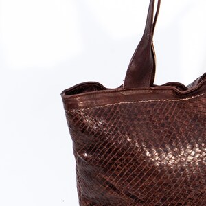 Puede incluir: Un bolso tote de cuero marr&oacute;n con un patr&oacute;n tejido. El bolso tiene dos asas largas.