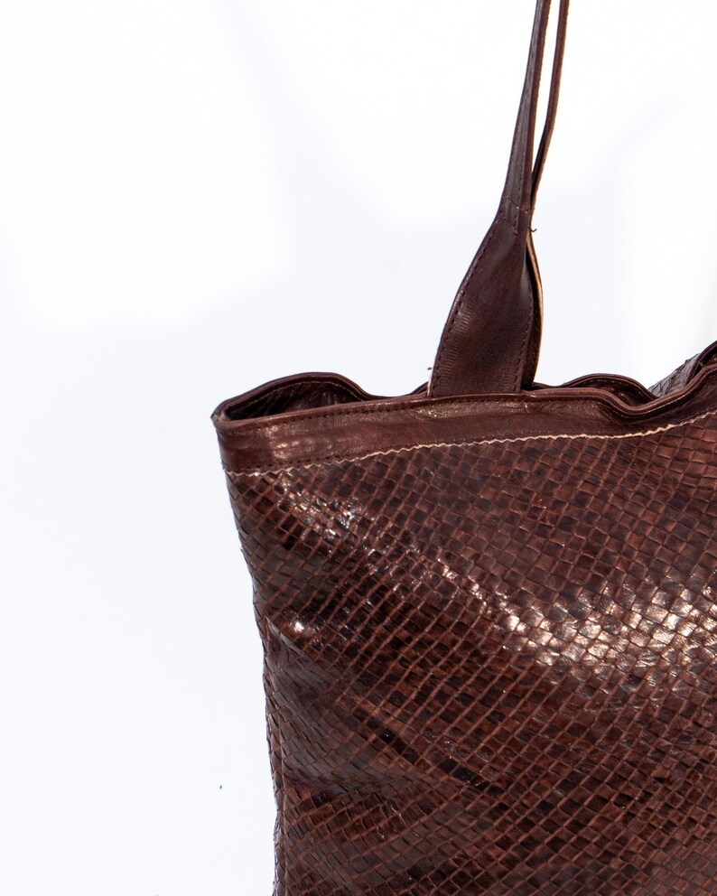 Puede incluir: Un bolso tote de cuero marr&oacute;n con un patr&oacute;n tejido. El bolso tiene dos asas largas.