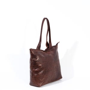 Puede incluir: Un bolso tote de cuero marr&oacute;n con un patr&oacute;n tejido. El bolso tiene una cremallera y dos asas superiores.