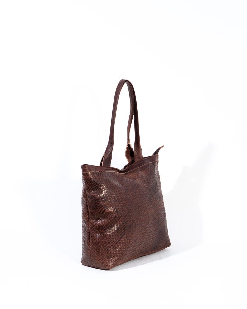 Puede incluir: Un bolso tote de cuero marr&oacute;n con un patr&oacute;n tejido. El bolso tiene una cremallera y dos asas superiores.