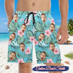 May include: Light blue beach shorts with a tropical floral pattern and faces. The shorts have a drawstring waist and the text "Custom Beach Shorts" in a cursive font.