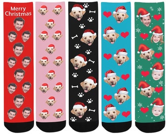 May include: Set of six Christmas themed socks featuring different patterns. One pair features a red background with repeated images of a man's face. Another pair features a pink background with repeated images of a dog wearing a Santa hat. Another pair features a black background with repeated images of a dog wearing a Santa hat and paw prints. Another pair features a blue background with repeated images of a dog wearing a Santa hat and hearts. Another pair features a green background with repeated images of a dog wearing a Santa hat and snowflakes. The last pair features a green background with repeated images of a baby wearing a Santa hat and snowflakes.