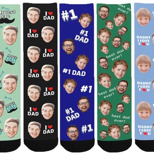 May include: Six pairs of colourful socks with different designs. The socks feature a repeated pattern of faces and text. The text on the socks includes "I love Dad", "#1 Dad", "Best Dad Ever!" and "Daddy I Love You".