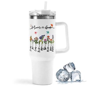 Puede incluir: Taza de viaje de acero inoxidable blanca con asa negra y tapa. La taza tiene un dise&ntilde;o floral con mariposas y el texto "Mom's Garden".