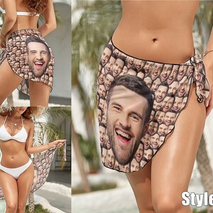May include: A woman wearing a white bikini top and bottom is wearing a sarong with a pattern of many faces. The sarong is tied at the side and the woman is standing in front of a tropical background. The text "Style 1" is visible in the bottom right corner of the image.