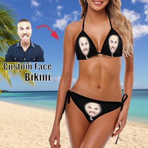 May include: A black bikini with a zipper detail. The zipper is open and a face is visible inside the zipper. The bikini is on a model standing on a beach.
