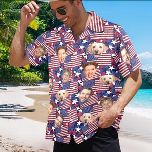 May include: Short-sleeved shirt featuring a repeating pattern of the American flag, white stars, and faces. The shirt is red, white, and blue. The shirt is worn by a person on a beach.
