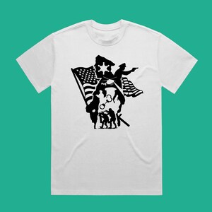 K&ouml;nnte beinhalten: Wei&szlig;es T-Shirt mit einem schwarzen Silhouetten-Design eines Polizisten, Soldaten und einer amerikanischen Flagge.