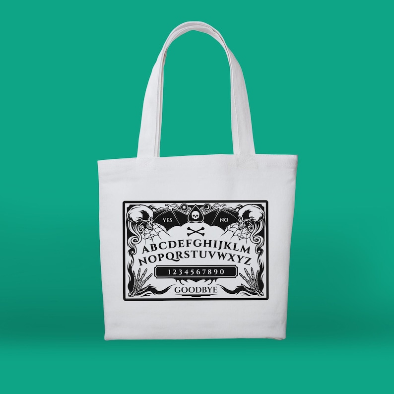 May include: White canvas tote bag with a black and white graphic of a Ouija board. The board features the letters A-Z, numbers 0-9, and the words "YES", "NO", and "GOODBYE".