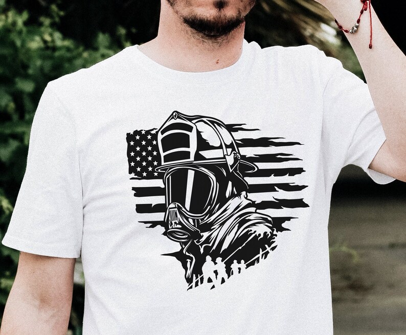May include: White t-shirt featuring a black and white graphic of a firefighter wearing a helmet and gas mask in front of an American flag.