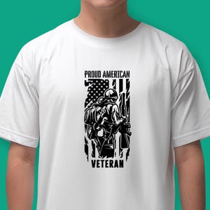 May include: White t-shirt with a black and white graphic of a soldier standing in front of an American flag. The text "Proud American Veteran" is printed on the shirt.