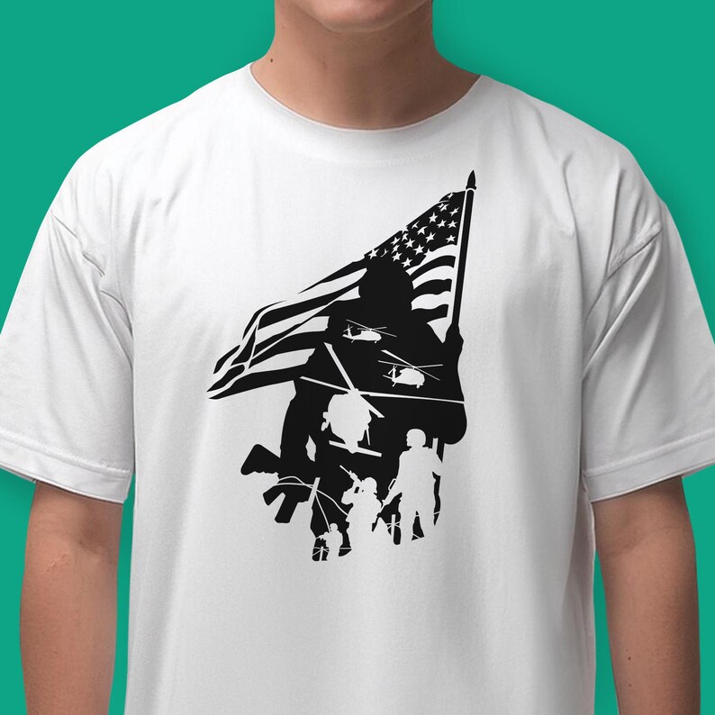 May include: A white t-shirt with a black silhouette of a soldier holding an American flag. The soldier is standing in front of a group of other soldiers, and there are helicopters flying overhead.