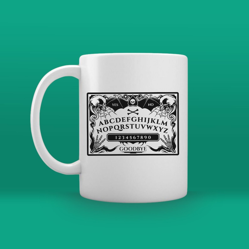 May include: White ceramic mug with a black and white image of a Ouija board. The board has the letters A-Z, numbers 0-9, and the words "YES", "NO", and "GOODBYE".