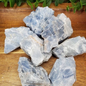 May include: A group of blue celestite crystal clusters on a wooden surface. The crystals are rough and have a natural, unpolished look.