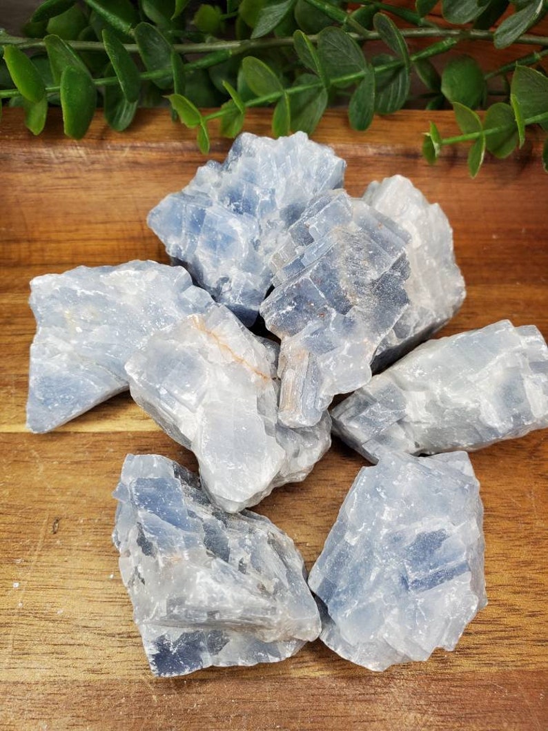 May include: A group of blue celestite crystal clusters on a wooden surface. The crystals are rough and have a natural, unpolished look.