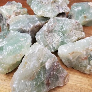 May include: A collection of rough, green fluorite crystals with brown inclusions. The crystals are various sizes and shapes, and have a translucent appearance.