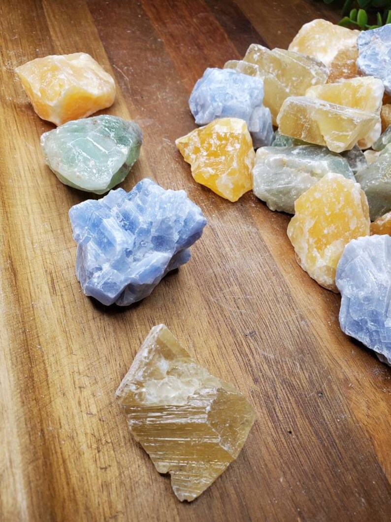 May include: A collection of raw, natural crystals in various shades of blue, green, and yellow. The crystals are arranged on a wooden surface.
