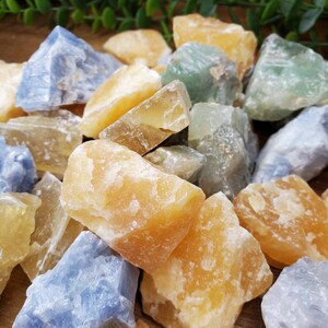 May include: A collection of rough, natural crystals in shades of blue, green, and yellow. The crystals are various sizes and shapes, and have a raw, unpolished look.