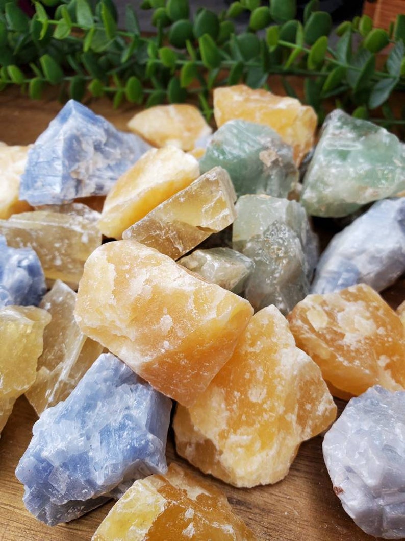 May include: A collection of rough, natural crystals in shades of blue, green, and yellow. The crystals are various sizes and shapes, and have a raw, unpolished look.