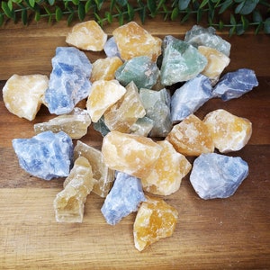 May include: A collection of rough, natural crystals in shades of blue, yellow, and green. The crystals are arranged on a wooden surface.