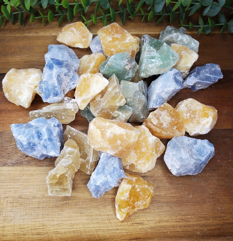 May include: A collection of rough, natural crystals in shades of blue, yellow, and green. The crystals are arranged on a wooden surface.