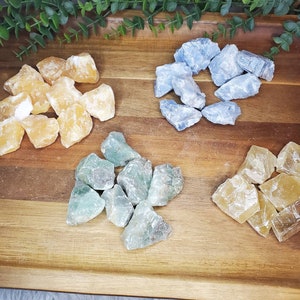 May include: A collection of four different types of crystals: yellow calcite, blue celestite, green fluorite, and a second type of yellow calcite. The crystals are arranged on a wooden surface.