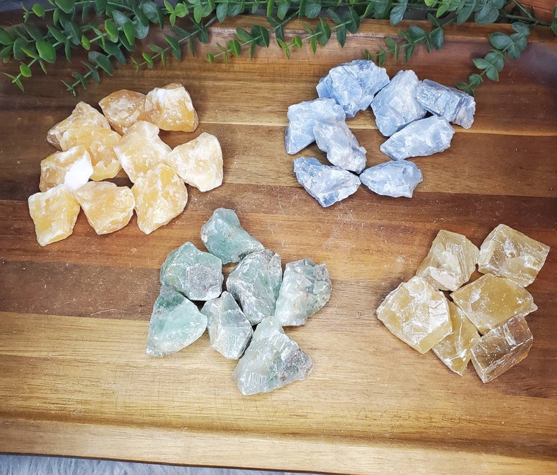 May include: A collection of four different types of crystals: yellow calcite, blue celestite, green fluorite, and a second type of yellow calcite. The crystals are arranged on a wooden surface.