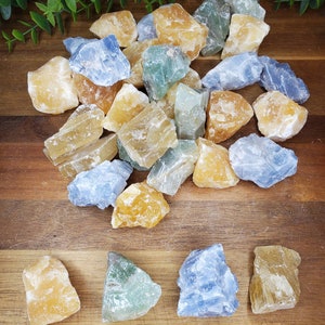 May include: A collection of raw, natural crystals in various shades of blue, yellow, and green. The crystals are arranged on a wooden surface.