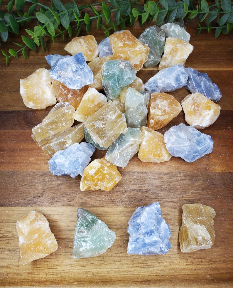 May include: A collection of raw, natural crystals in various shades of blue, yellow, and green. The crystals are arranged on a wooden surface.