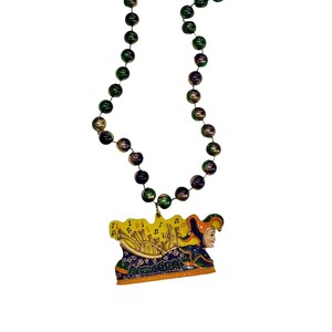 May include: A Mardi Gras necklace with iridescent green, gold, and purple beads. The pendant features a yellow background with musical notes and a jester's face. The jester is wearing a colorful hat and outfit.