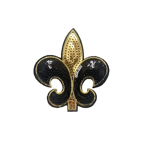May include: A black and gold sequined fleur-de-lis patch. The design features a gold center with black sequined accents and a gold border. The patch is likely for decorative purposes, such as on clothing or accessories.