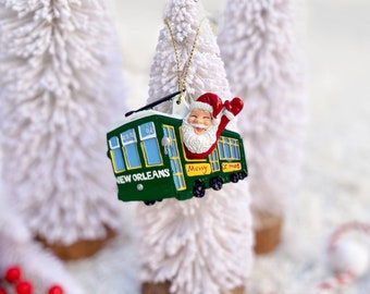 May include: Green and yellow New Orleans streetcar Christmas ornament with Santa Claus riding inside and waving. The ornament reads "Merry Xmas" and "New Orleans".