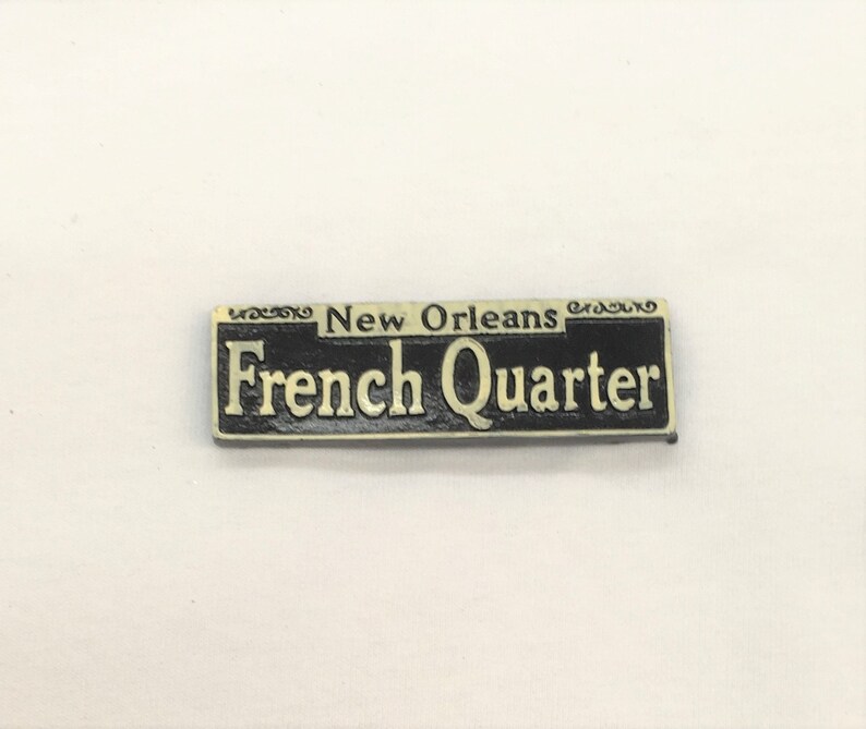 May include: A black and gold metal sign with the text "New Orleans French Quarter" in white lettering.