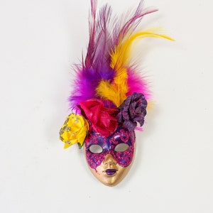 May include: A purple and gold masquerade mask with pink, yellow, and purple feathers and flowers.