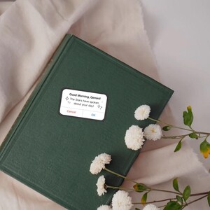 a sticker reminiscent of an iPhone alert, but it says, good morning, Gemini or other zodiac sign, the stars have spoken about your day! in reference to zodiac academy perfect for adding bookish flair to your kindle or laptop