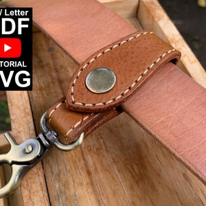 Puede incluir: Un cinturón de cuero marrón con un bucle de cuero cosido y un broche metálico. El bucle está unido a un llavero de latón.