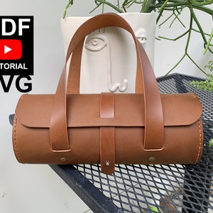 May include: A brown leather cylindrical handbag with two brown leather straps. The bag is sitting on a black metal table. The text "PDF TUTORIAL SVG File" is visible in the top left corner of the image.