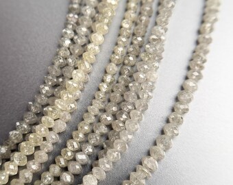 May include: Strands of raw, uncut diamond beads in varying sizes. The beads are a mix of clear and light grey, with a faceted, irregular shape. The strands are arranged in a cascading pattern against a neutral background.