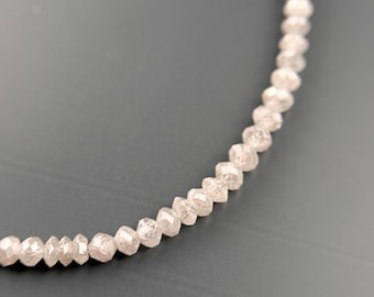 May include: A strand of faceted, light-colored beads, possibly gemstones, curves across a dark gray background. The beads have a slightly irregular shape and a subtle sparkle, suggesting a natural material.