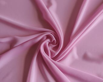 Könnte beinhalten: Nahaufnahme eines zarten, hellrosa Stoffes, der kunstvoll drapiert und gewirbelt ist. Die Falten des Stoffes erzeugen Schatten, die seine glatte Textur hervorheben. Das Bild unterstreicht die Fließfähigkeit und Weichheit des Stoffes.