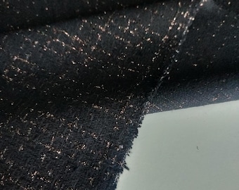May include: Close-up of a black fabric with a textured weave. The fabric is speckled with small, shimmering gold threads, creating a subtle sparkle effect. The material is folded, revealing its layered construction.