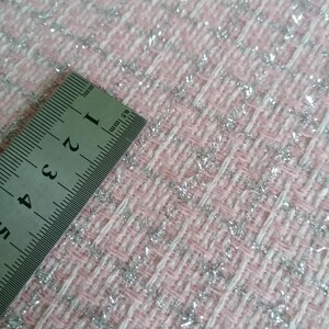 May include: Close-up of a pink and white fabric with silver glitter woven into the fabric. A ruler is placed on the fabric, showing measurements in inches.