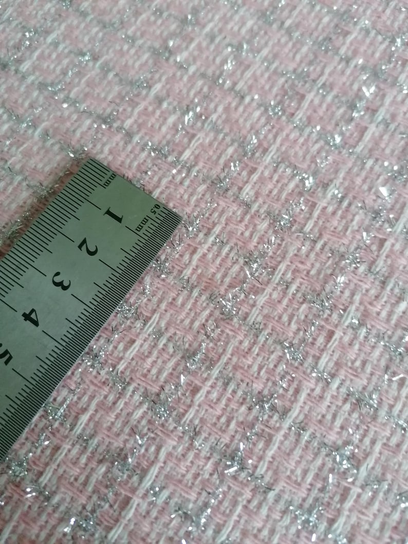 May include: Close-up of a pink and white fabric with silver glitter woven into the fabric. A ruler is placed on the fabric, showing measurements in inches.