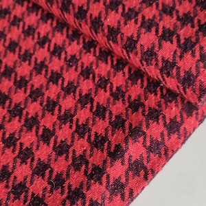 Könnte beinhalten: Nahaufnahme eines gefalteten Stoffes mit einem rot-schwarzen Hahnentrittmuster. Der Stoff ist strukturiert und scheint ein gewebtes Material zu sein, wobei sich das Muster über die Oberfläche wiederholt. Die Farben sind lebendig.
