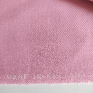 Può includere: Primo piano di un tessuto rosa con un'etichetta bianca che recita "MADE IN ENGLAND".