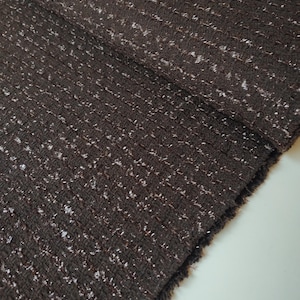May include: A dark brown fabric with a textured weave featuring intermittent white flecks throughout the material. The textile displays a folded edge with a slightly frayed border, showcasing a dense, woven pattern with a consistent color palette.